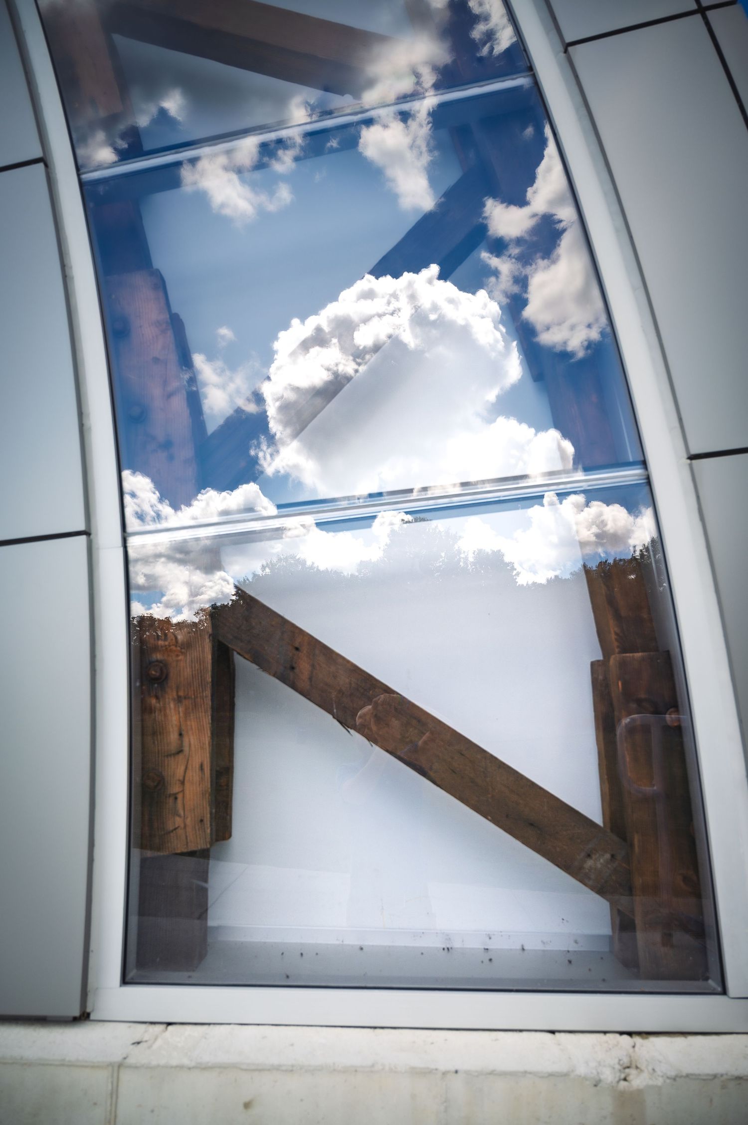 Sequence of skylight windows showing wooden beams against a bright blue sky with white fluffy clouds.