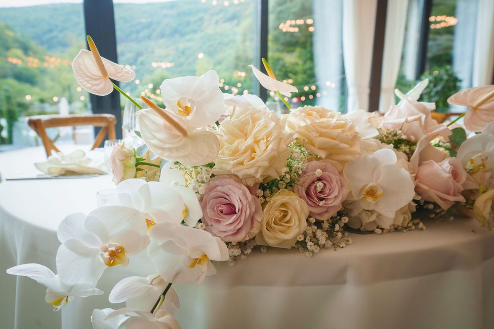 A decorative floral arrangement featuring pink roses and white orchids adorns an elegant wedding reception table.