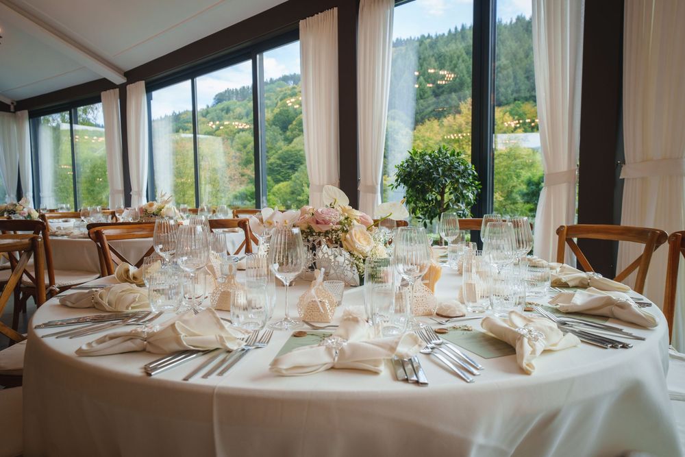 Elegant wedding reception table setting with white linens and glassware in a bright room with panoramic mountain views.