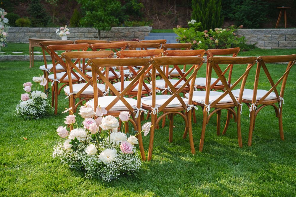 Wooden cross-back chairs arranged in rows with white floral arrangements for an outdoor garden wedding ceremony.
