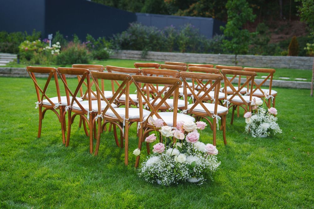 Wooden folding chairs arranged in rows on green grass with white floral arrangements for an outdoor wedding ceremony.