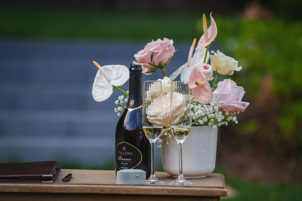 Wine bottle and glass next to a delicate floral arrangement with pink and white roses on a rustic wooden surface.