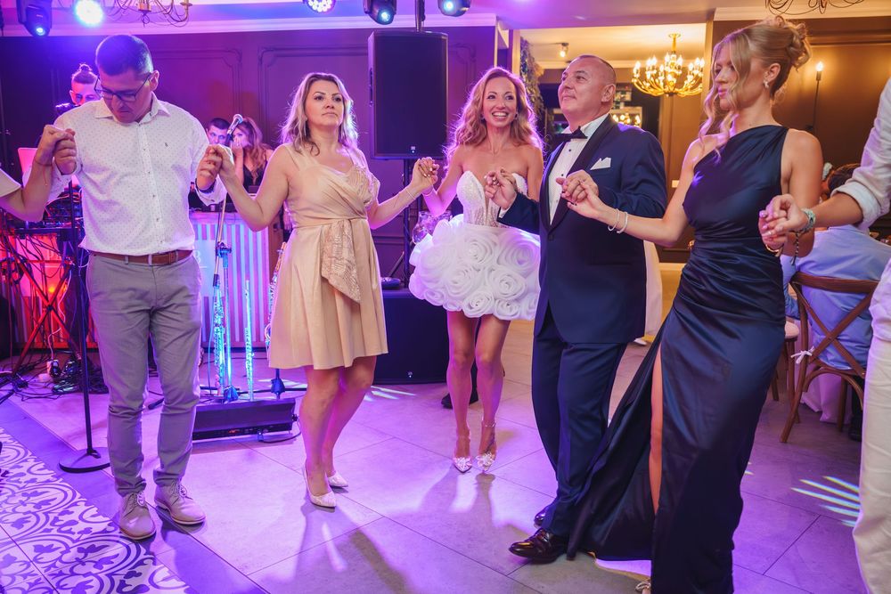 Wedding guests dance together on a purple-lit dance floor during an evening reception celebration.
