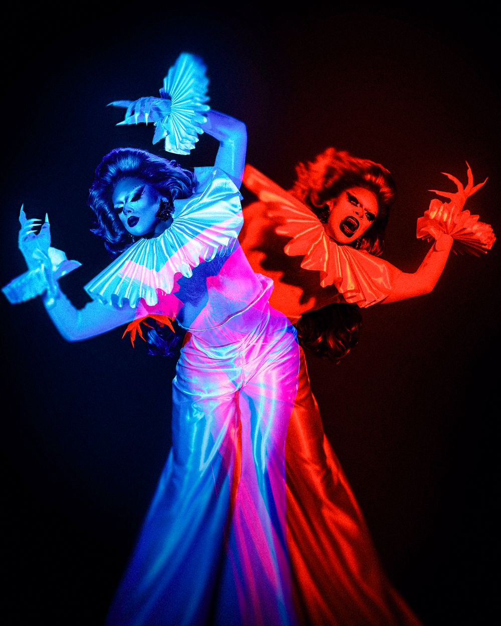 Artistic dancers in flowing costumes illuminated by contrasting blue and red lighting create dramatic silhouettes against dark background.