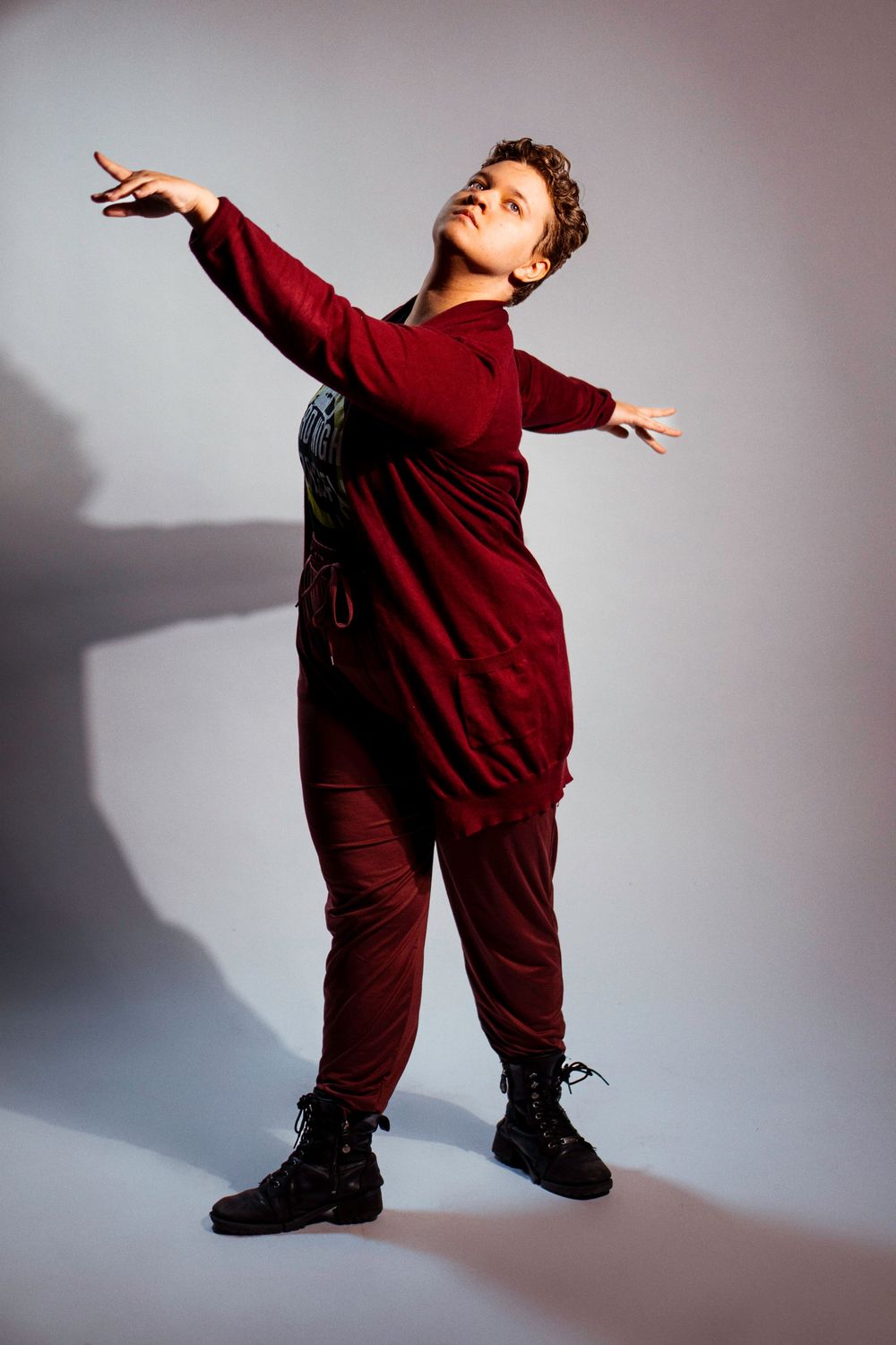 A person in a burgundy outfit strikes dynamic dance poses against a light background with dramatic shadows.