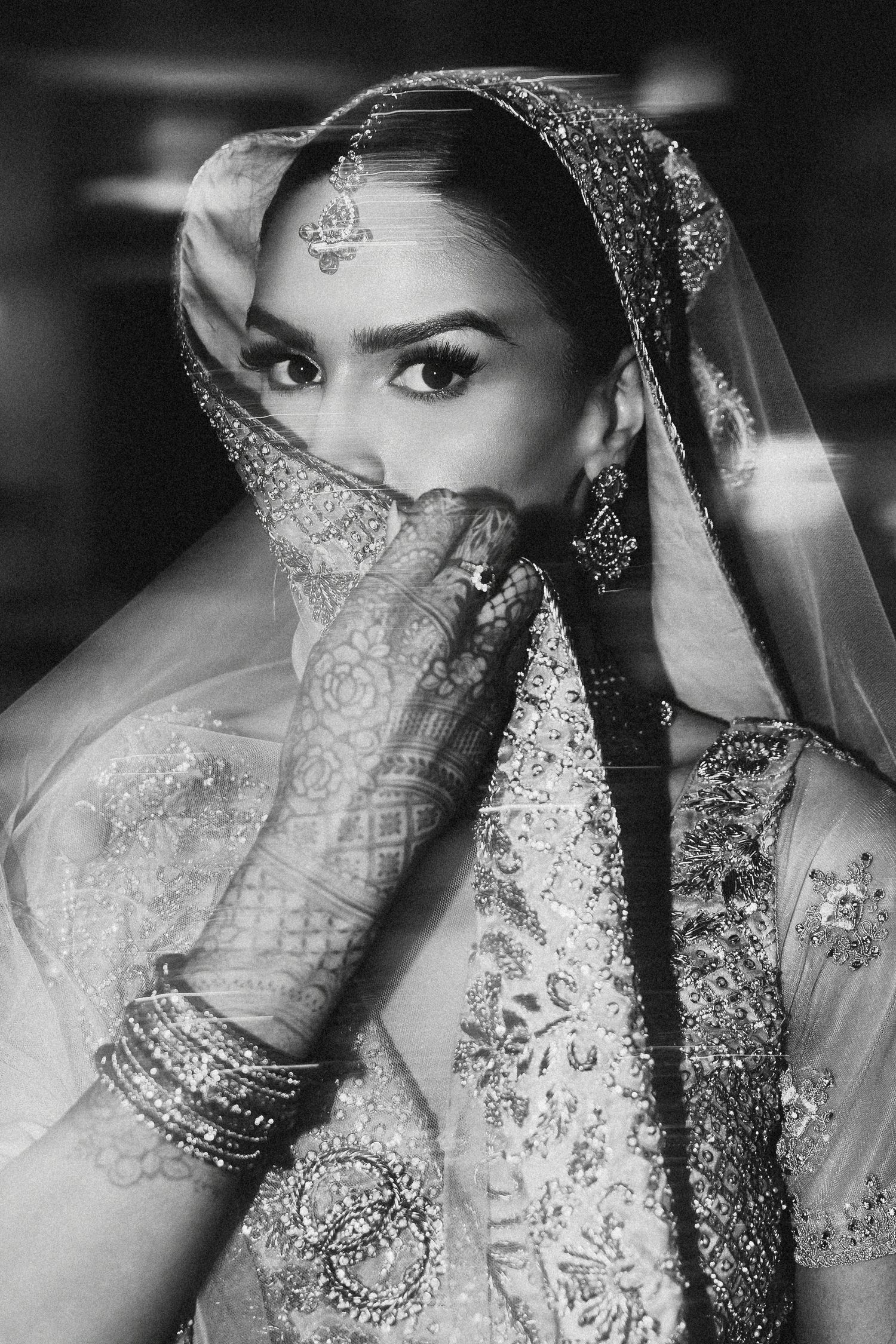 Editorial style portrait of Muslim bride covering her face with dupatta, showcasing intricate henna designs and traditional bridal jewelry