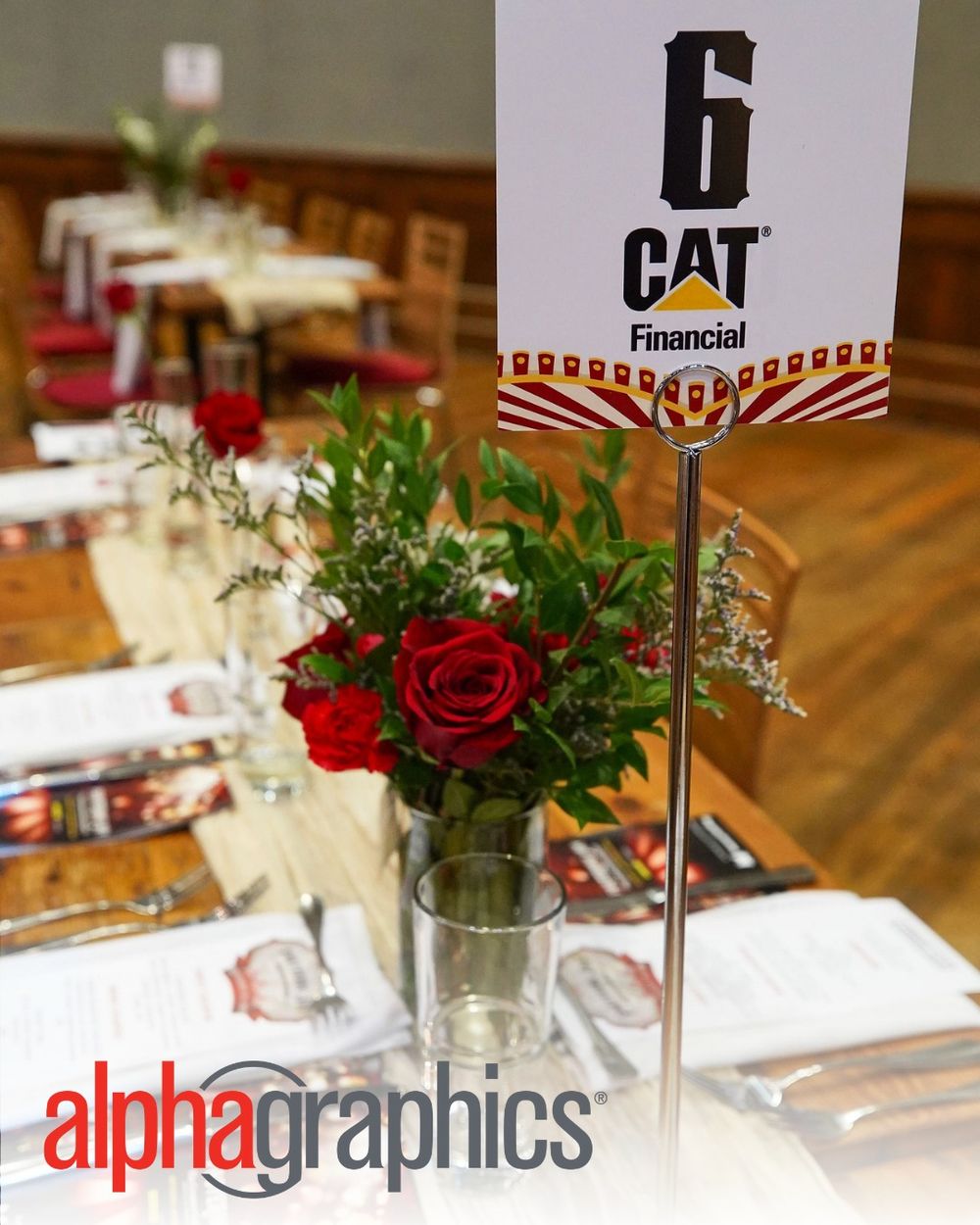Corporate event table setting with CAT Financial branding and red rose centerpiece.