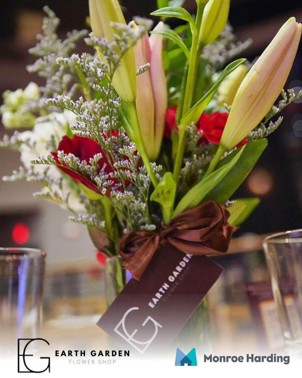 Elegant floral arrangement with lilies and red flowers tied with brown ribbon from Earth Garden.