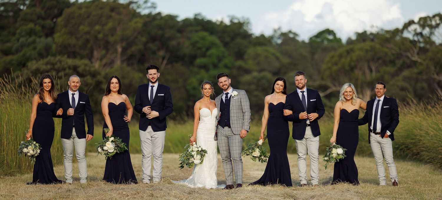 Wedding party poses together outdoors in navy and grey attire with green bouquets.