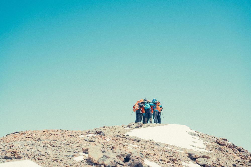 A series of panoramic photos showing hikers traversing a rugged mountain ridge against a bright blue sky.