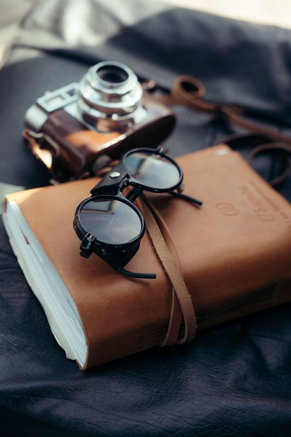 A vintage leather-bound journal with pocket watch photographed from multiple angles on dark fabric background.