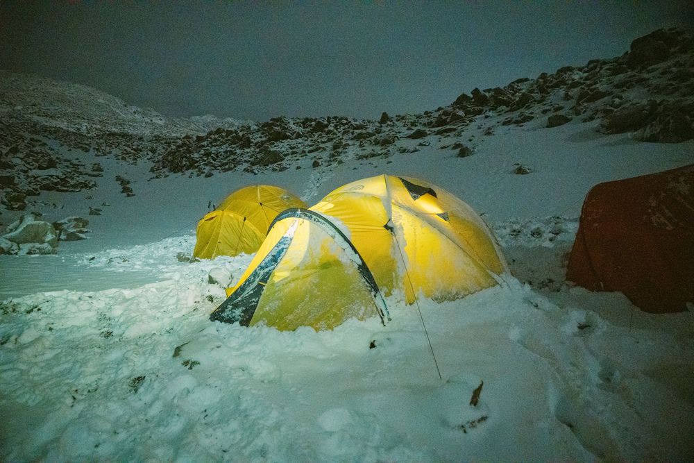 Yellow tents dot a snowy mountainous landscape during a winter expedition in harsh alpine conditions.
