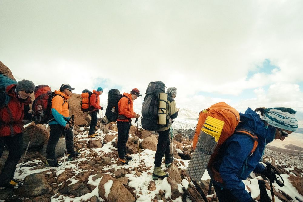 Mountain climbers with heavy backpacks traverse rocky terrain during a challenging alpine expedition.