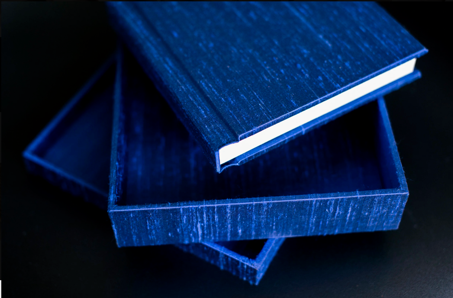 Three stacked hardcover books with rich blue textured covers against a black background.