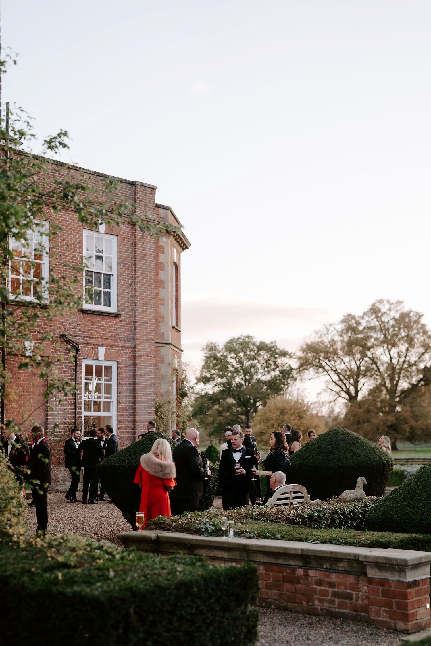 wedding guests enjoying the setting sun in the gardens outside Iscoyd park