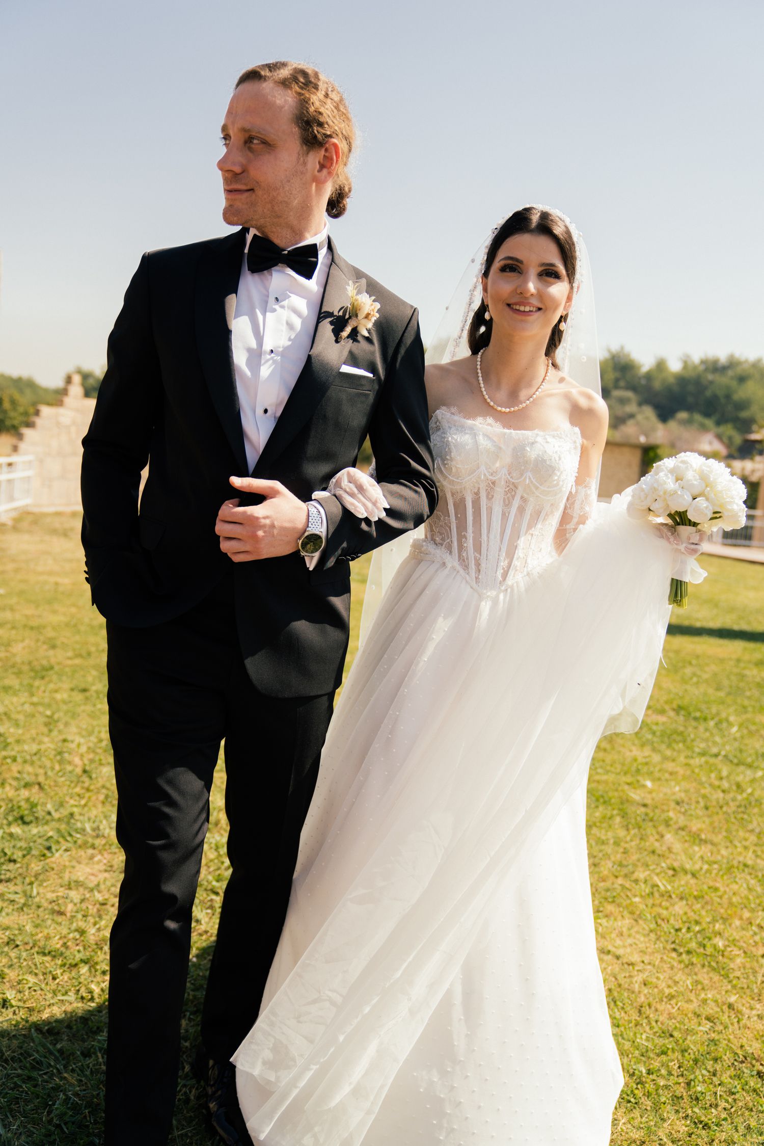 Newlyweds walking together on grassy hillside in formal wedding attire.