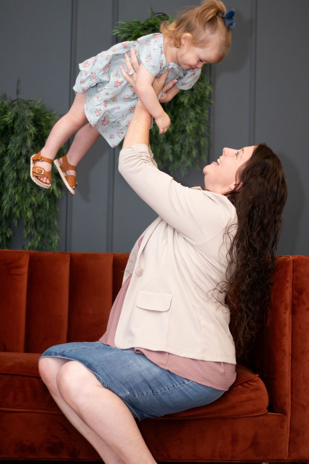 Parent and child share a joyful moment playing together on a brown couch in a living room setting.