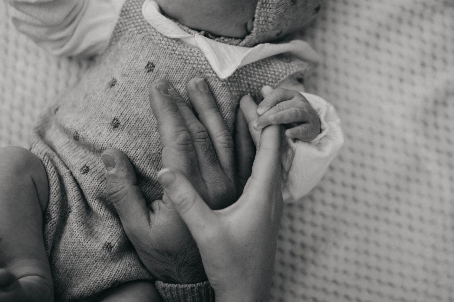 Manos de madre y padre sobre su bebé recién nacido en fotografía en blanco y negro en Vila-seca