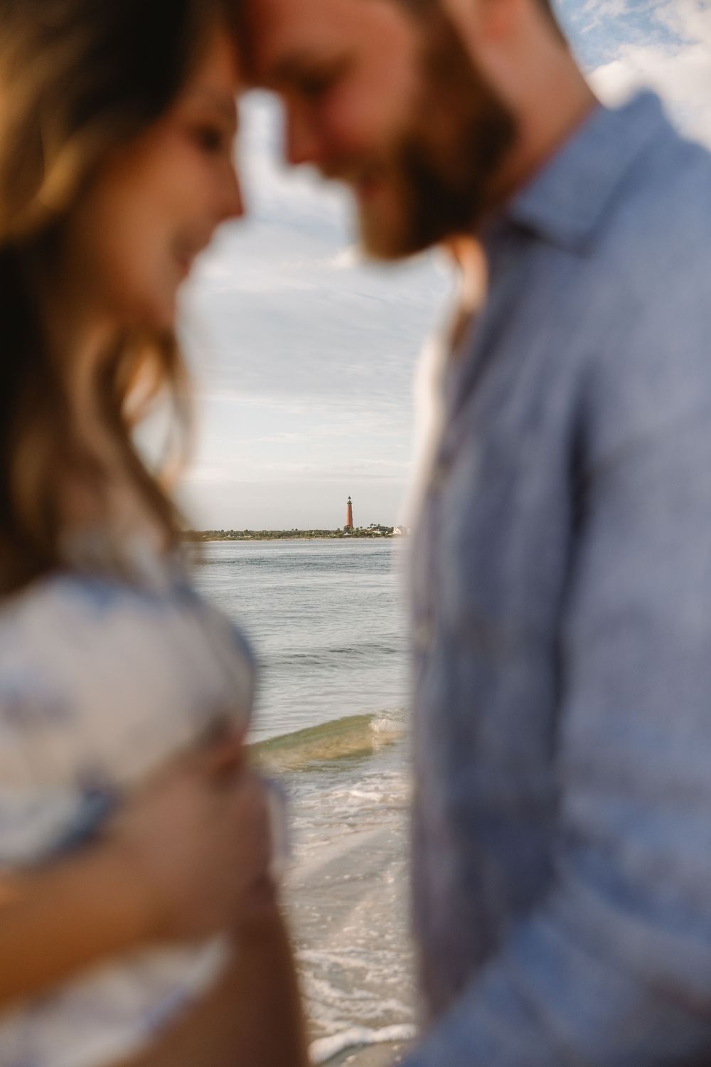 Intimate beachside portraits of a couple standing together with ocean waves and coastline in the background.