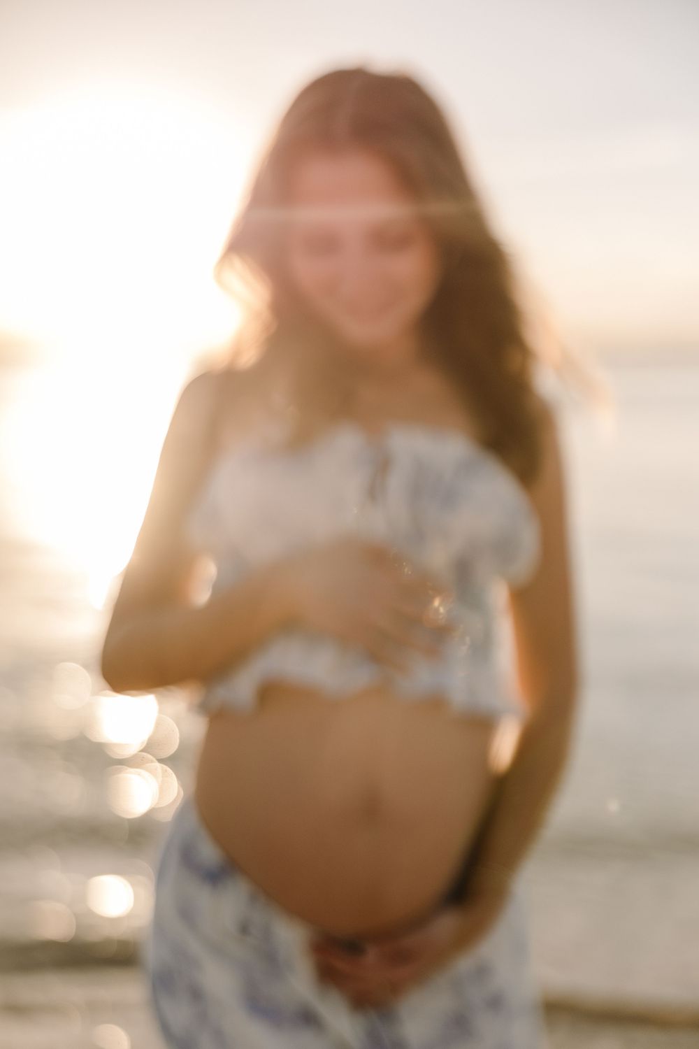 Silhouetted maternity photoshoot at sunset with golden light illuminating a floral dress.