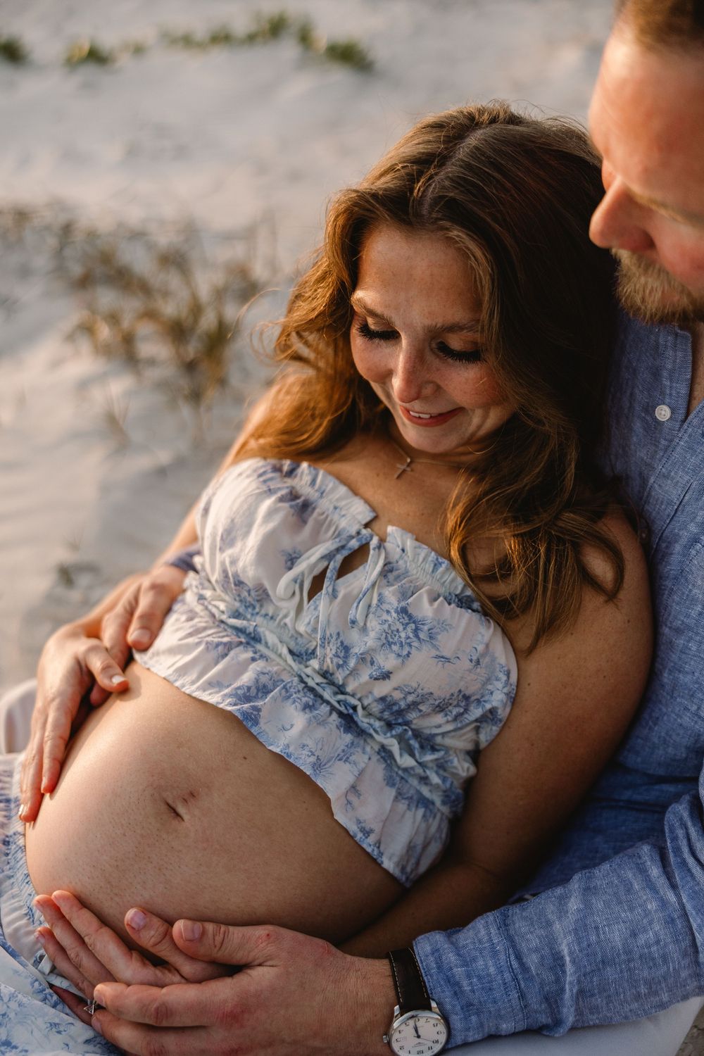 Intimate maternity photoshoot showing couple embracing on beach at sunset in soft natural light.
