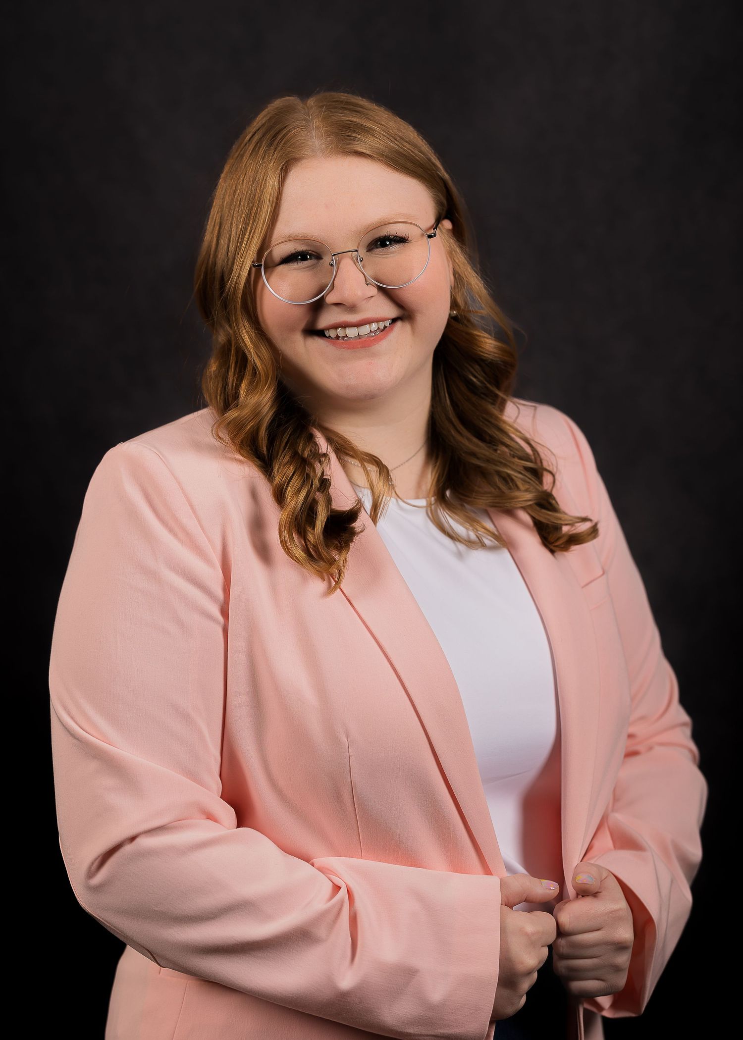 Professional headshot against black background wearing pink blazer and white top with warm smile.