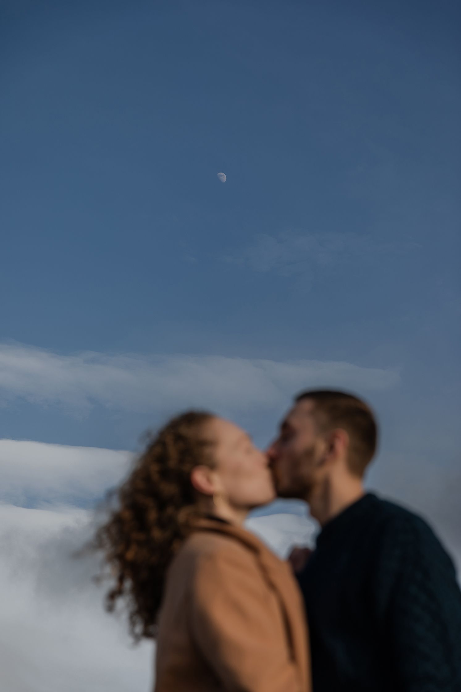 Romantic Ireland travel couple session captured at sunset along coastal cliffs, couple kissing with moon shining above their heads