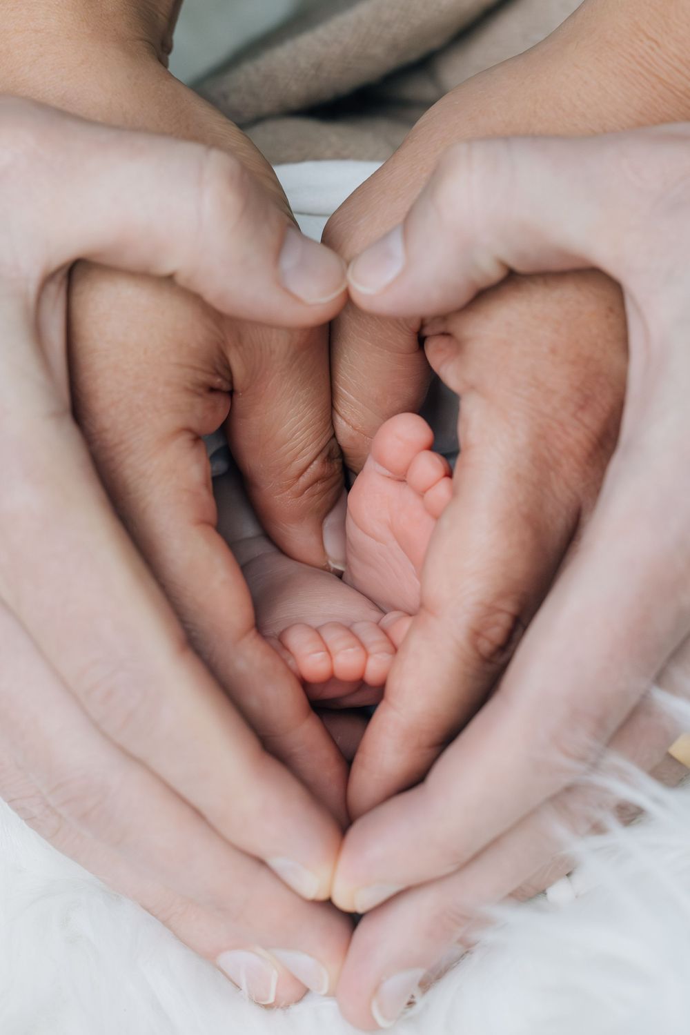 Parents forming a heart shape with their hands around their newborn baby's tiny feet.