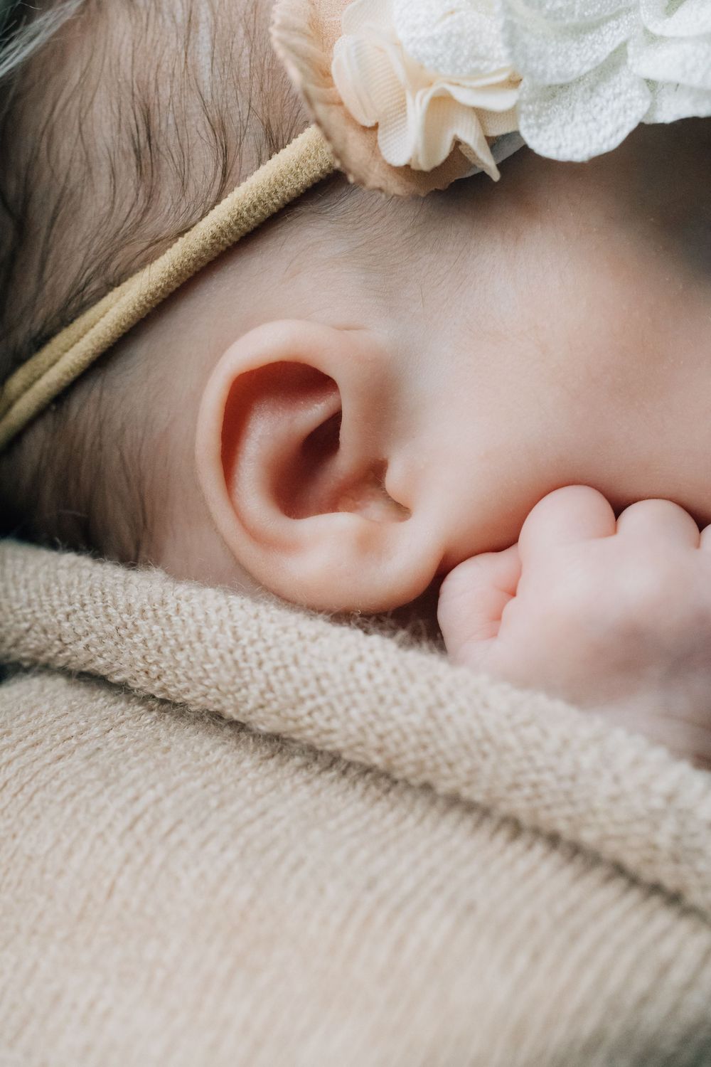 Close-up of sleeping newborn baby's ear and tiny hand with floral headband.