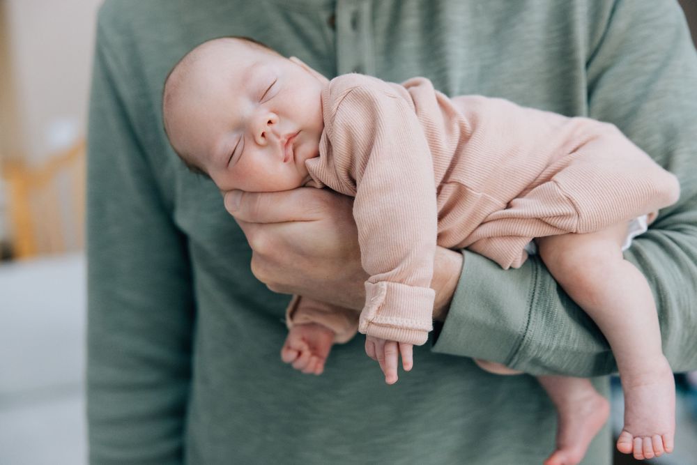 Sleeping newborn baby in pink outfit cradled in one arm.