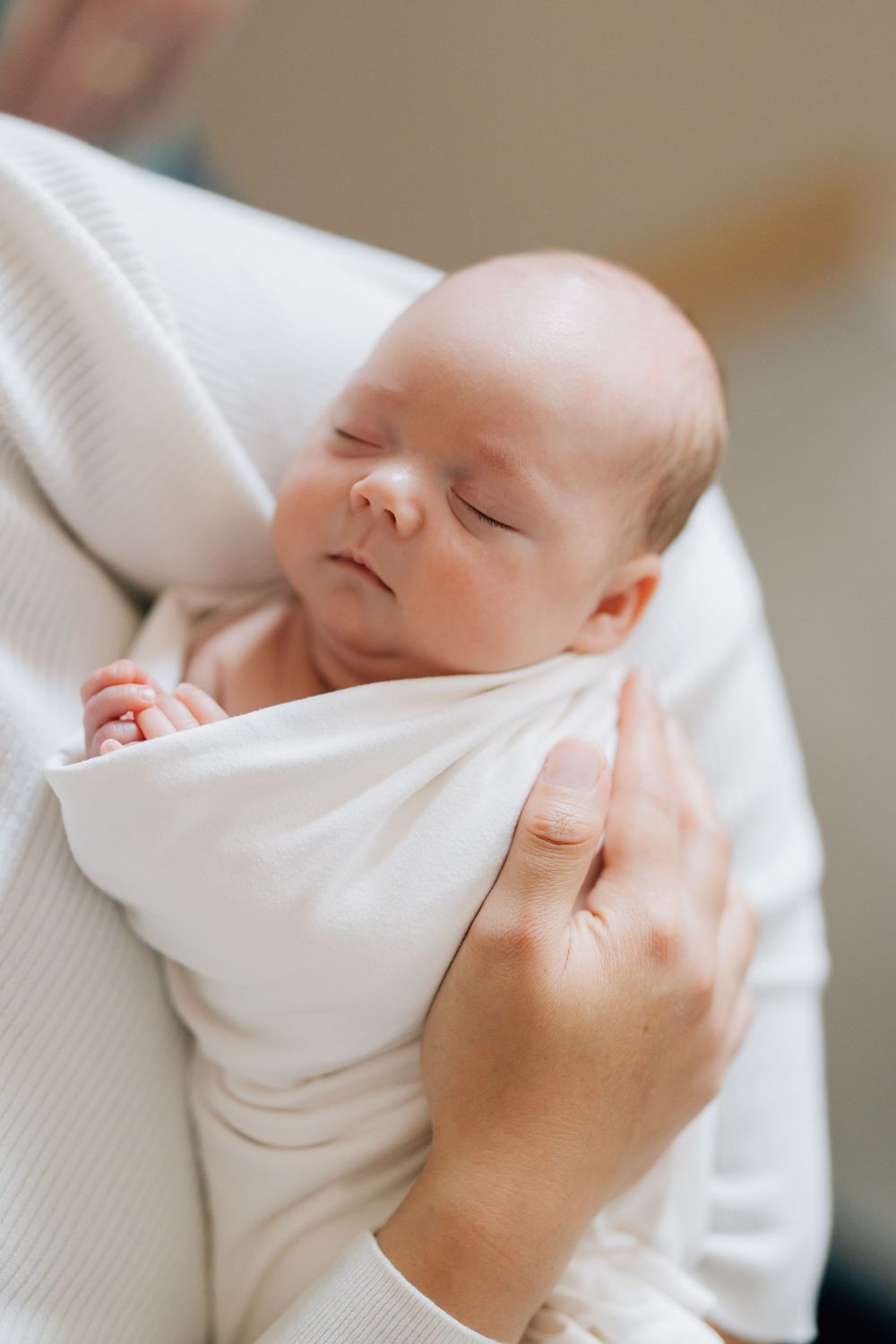 Peaceful sleeping newborn baby swaddled in white cloth held gently.