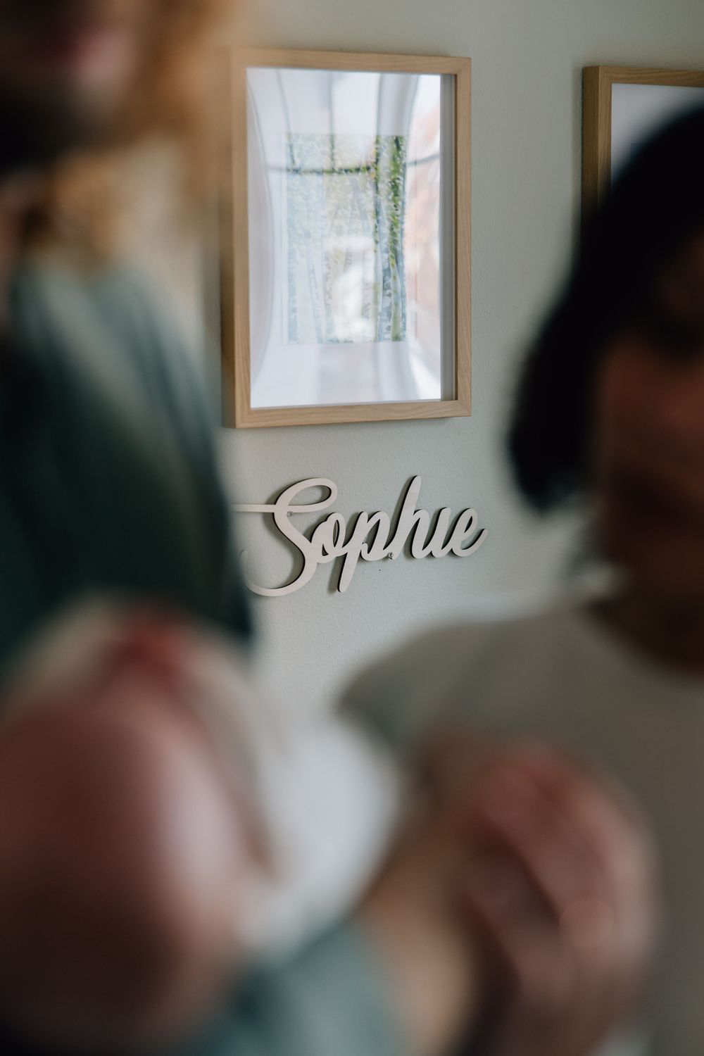 Wooden name sign spelling Sophie on nursery wall with parents.