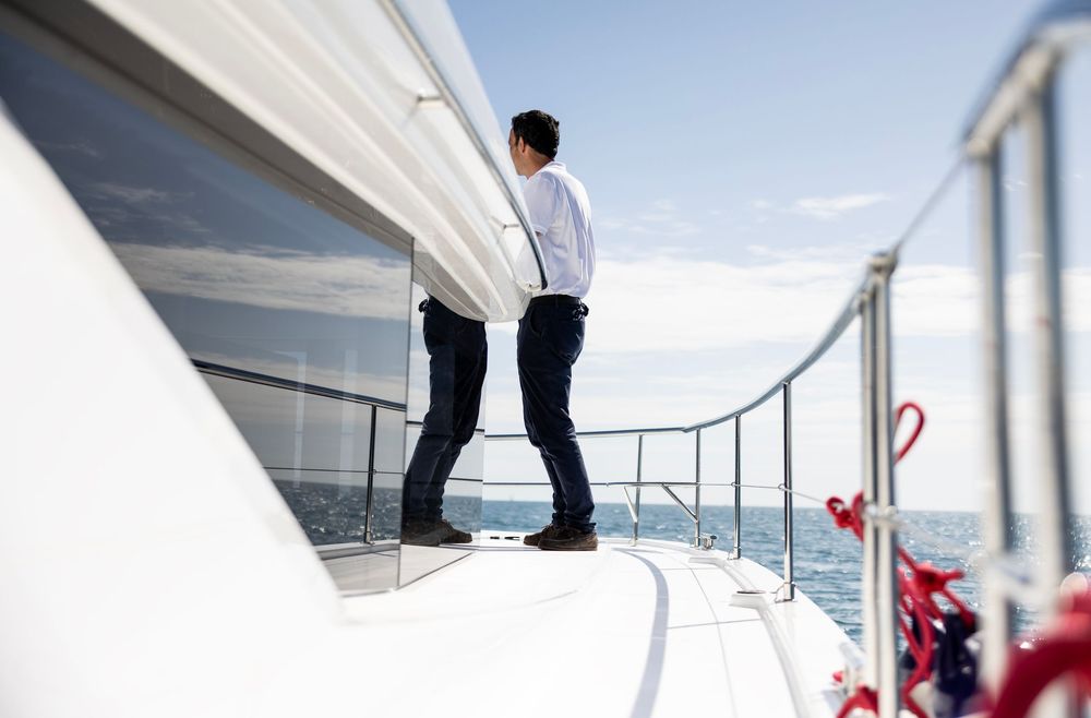 Man in suspenders standing on yacht deck gazing at open sea on sunny day.