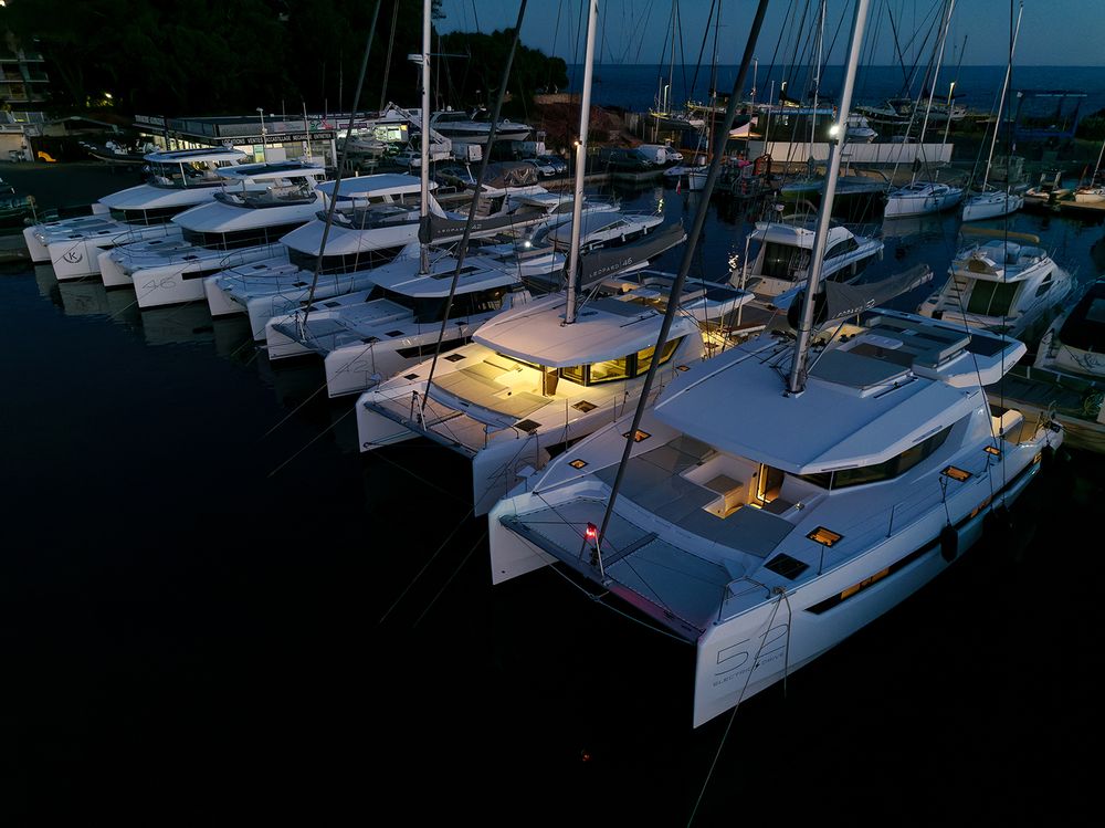 Aerial view of sailboats and catamarans moored at a marina dock during sunset.