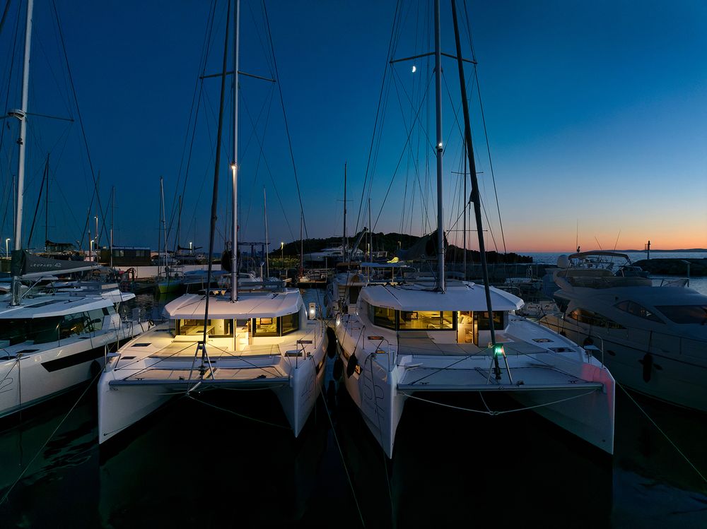 Silhouettes of sailboat masts at sunset with deep blue sky and orange horizon.
