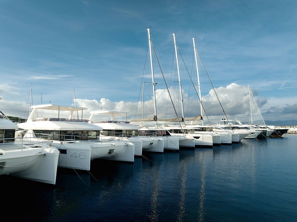 Row of white catamarans anchored in a calm blue harbor under bright sunny skies.