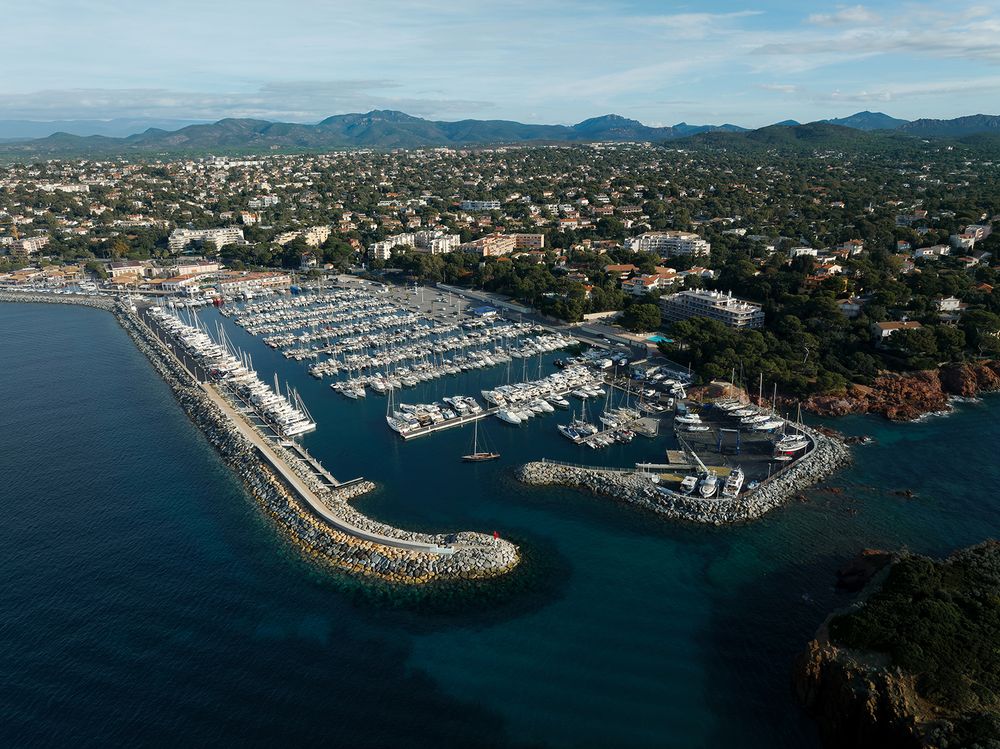 Panoramic aerial view of a coastal marina with mountains and residential areas in the background.