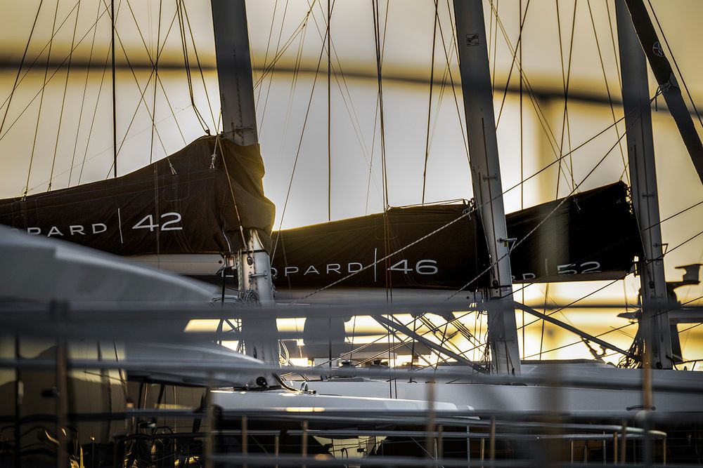 Silhouetted masts and rigging of sailboats against a bright cloudy sky at a marina.