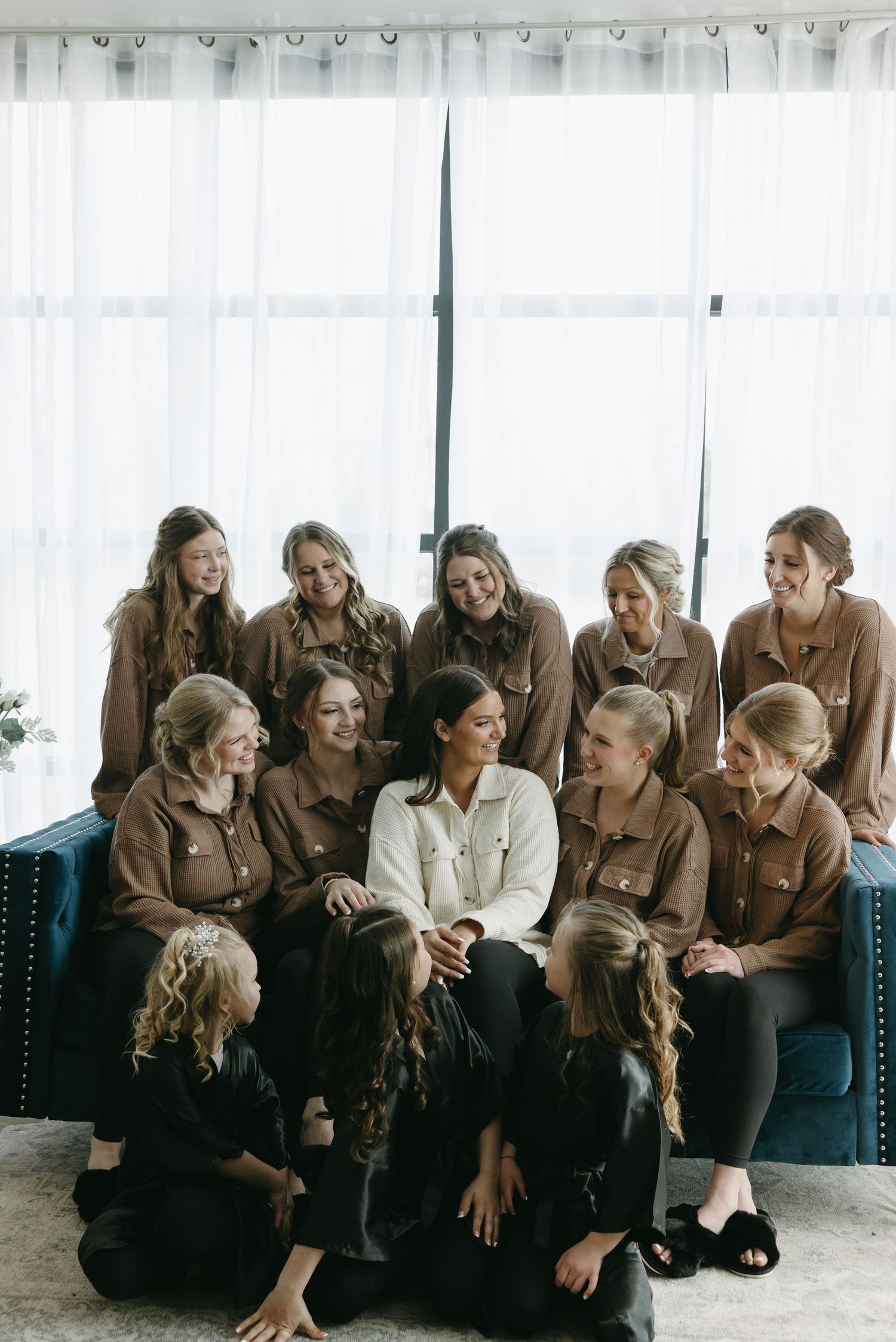 Group of bridesmaids in matching brown outfits pose together on blue couch.