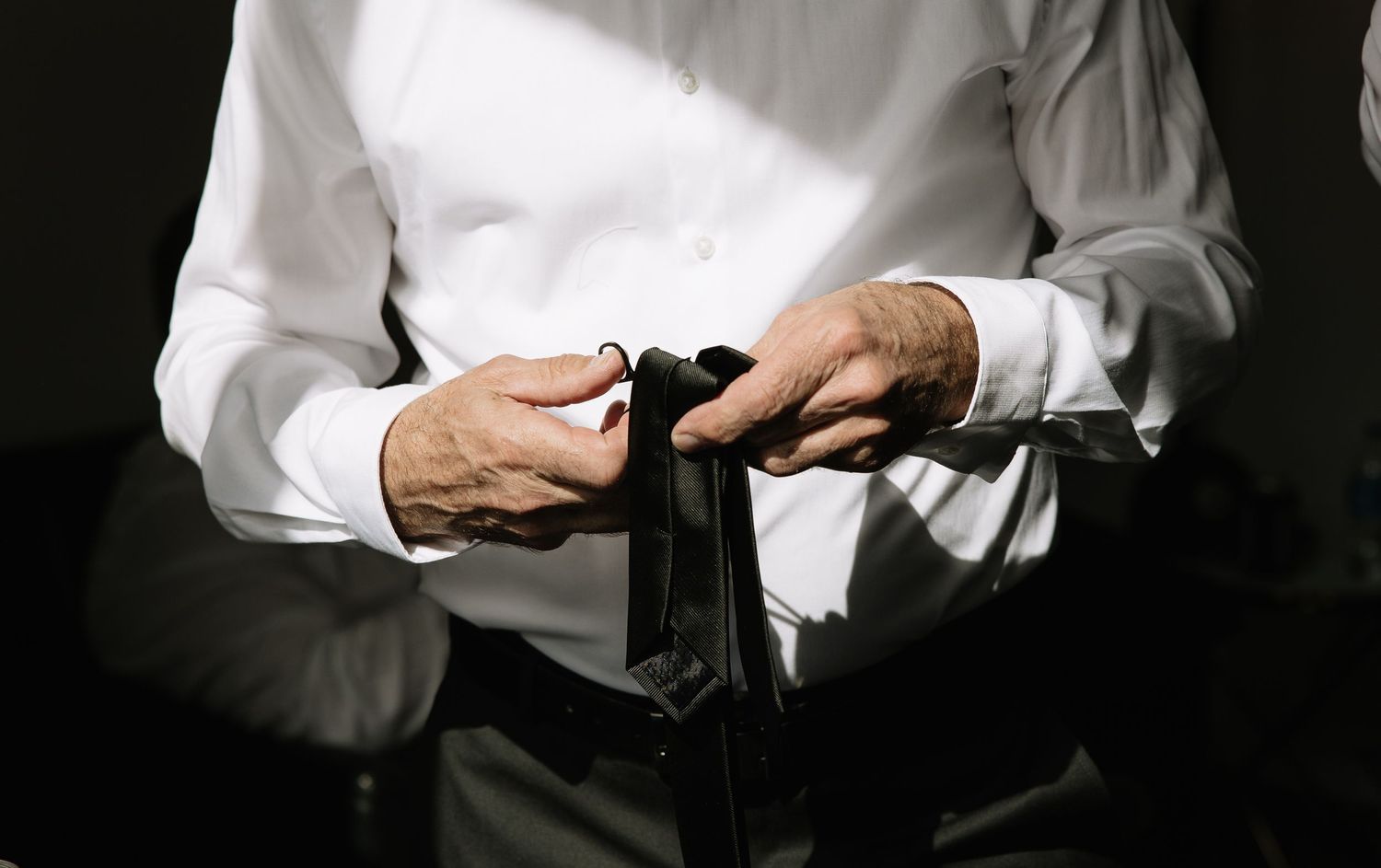 Close-up of hands adjusting formal black tie in dramatic lighting.