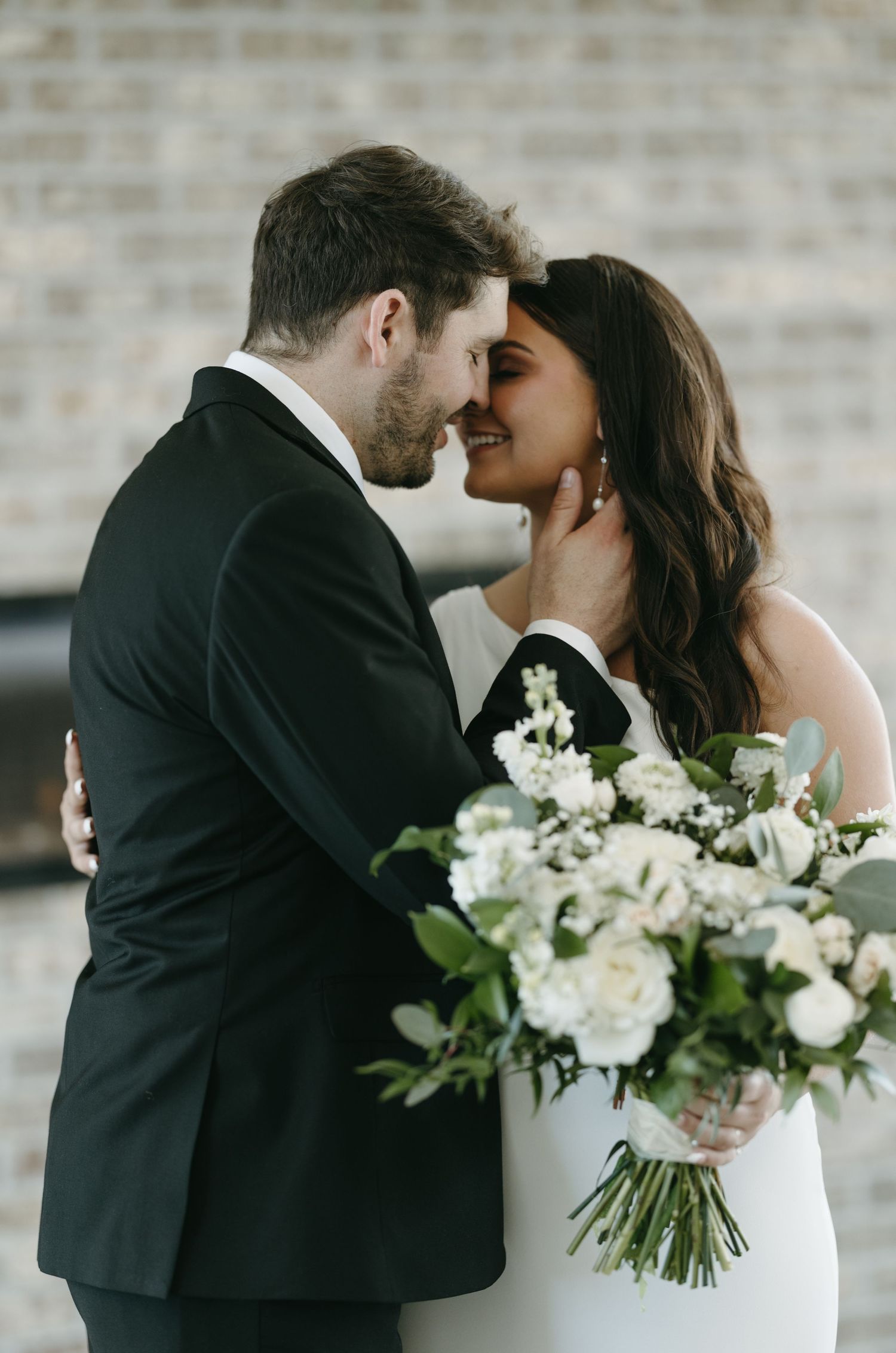 A romantic moment between newlyweds as they hold a beautiful white floral bouquet.