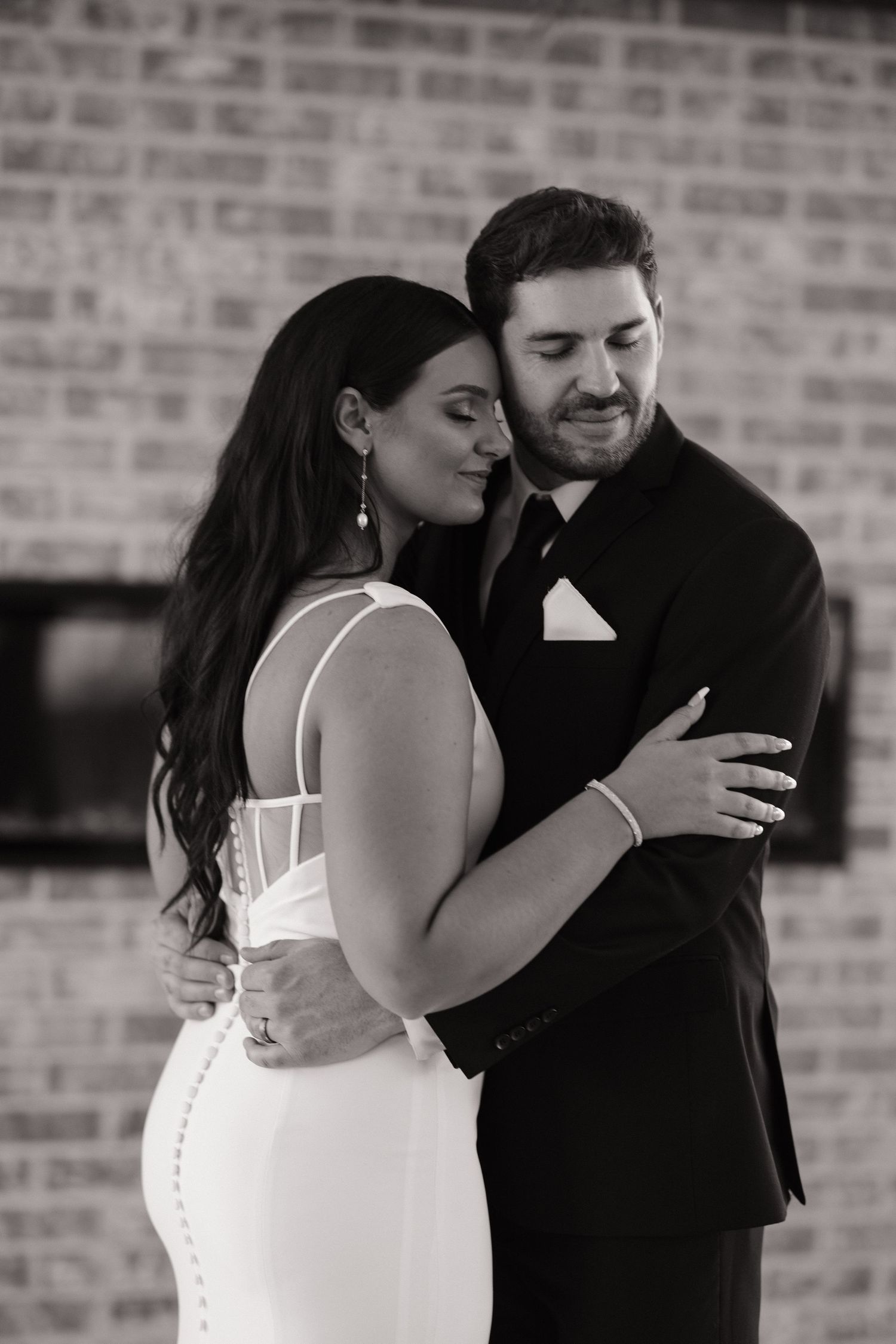 A tender black and white portrait of newlyweds sharing an intimate moment against a brick wall.
