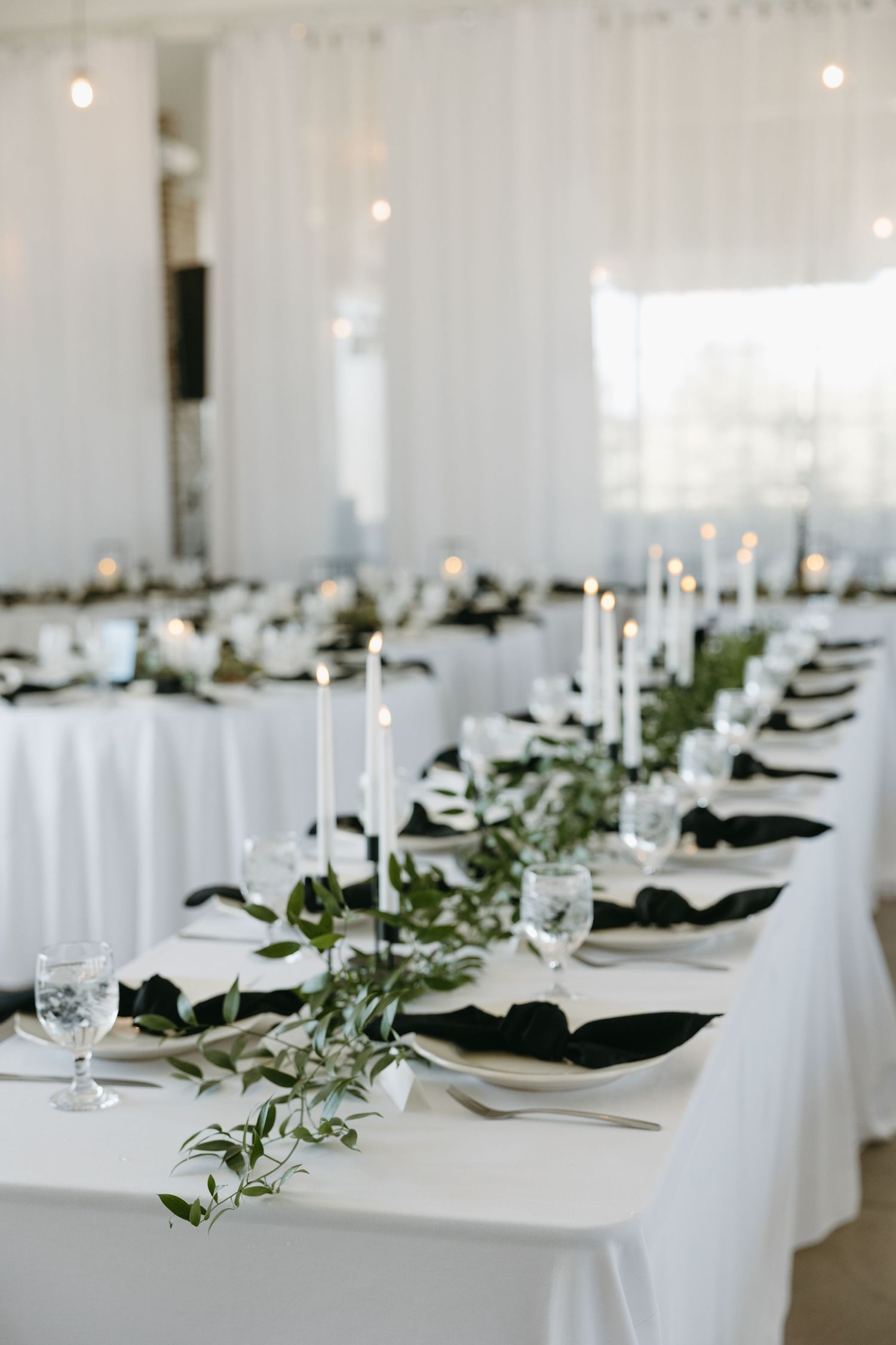An elegant wedding reception table setting with white linens, taper candles, and delicate greenery.