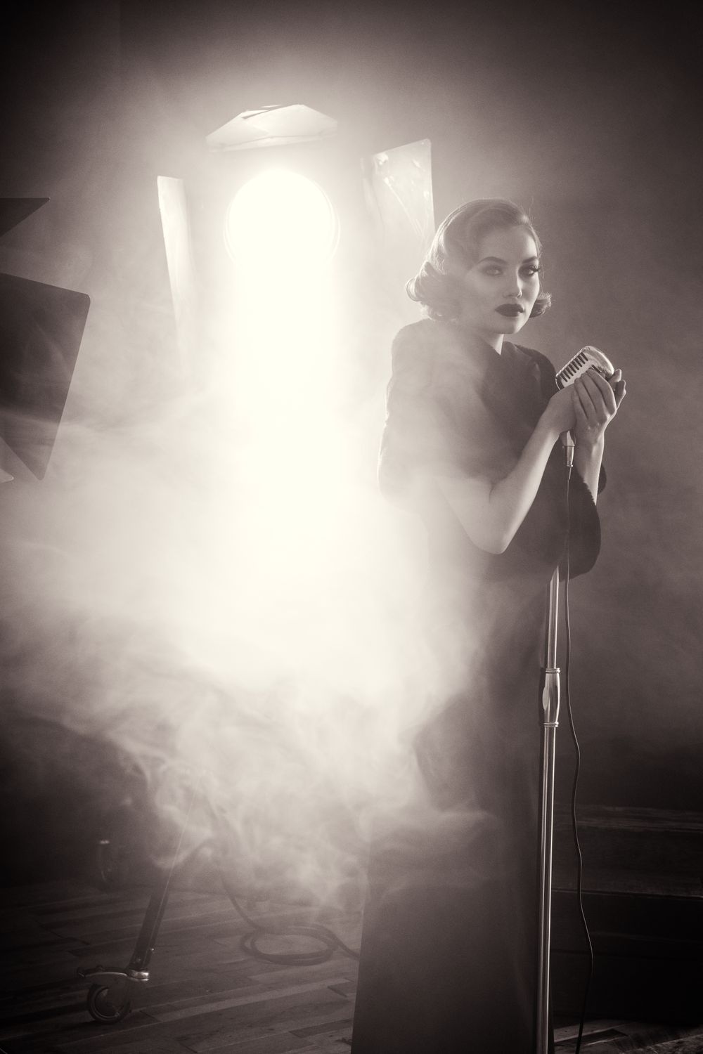 Atmospheric black and white photo of a performer singing on stage surrounded by dramatic lighting and fog.