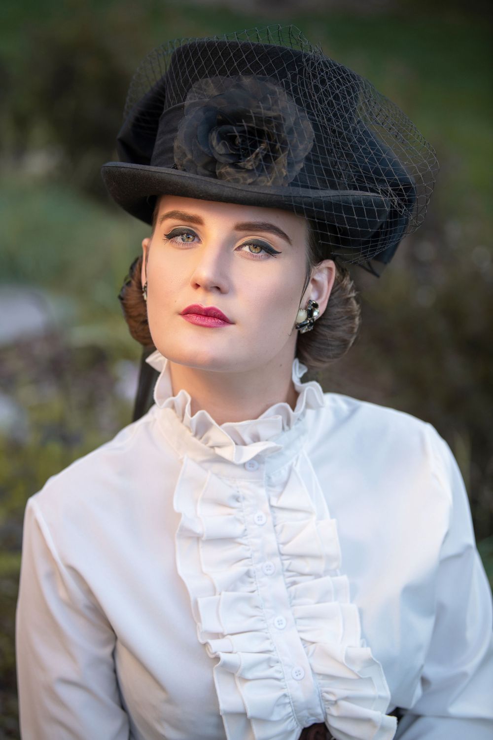Victorian-style portrait featuring black hat with mesh veil and white ruffled blouse.