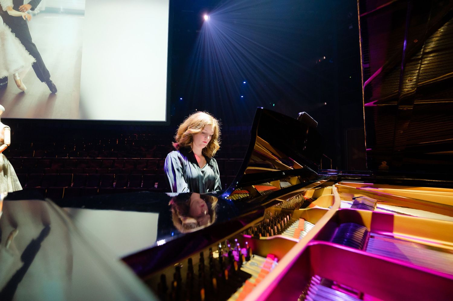 Musician performs on grand piano under dramatic purple stage lighting.
