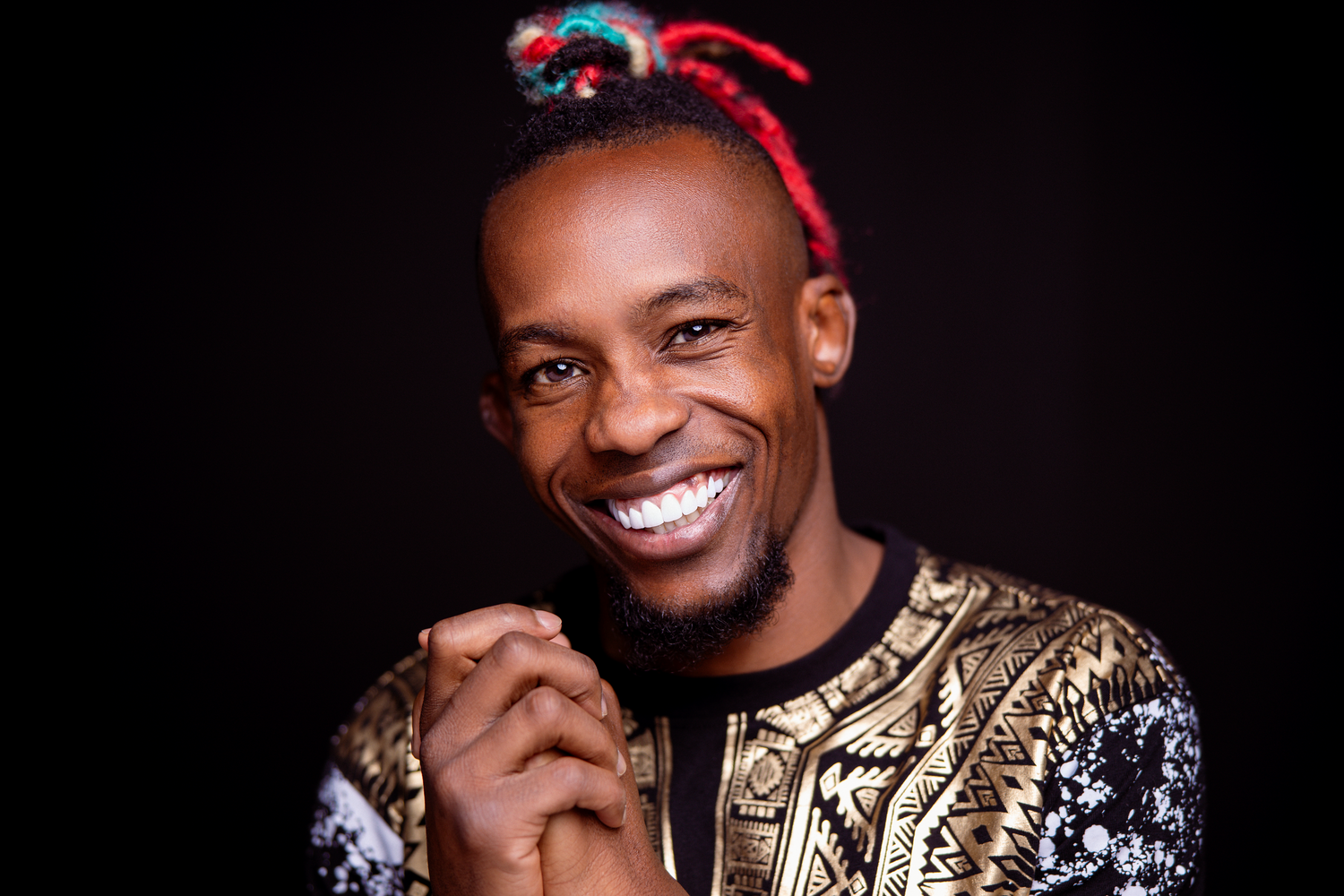 Person in festive red headband and gold patterned top smiles brightly against dark background.
