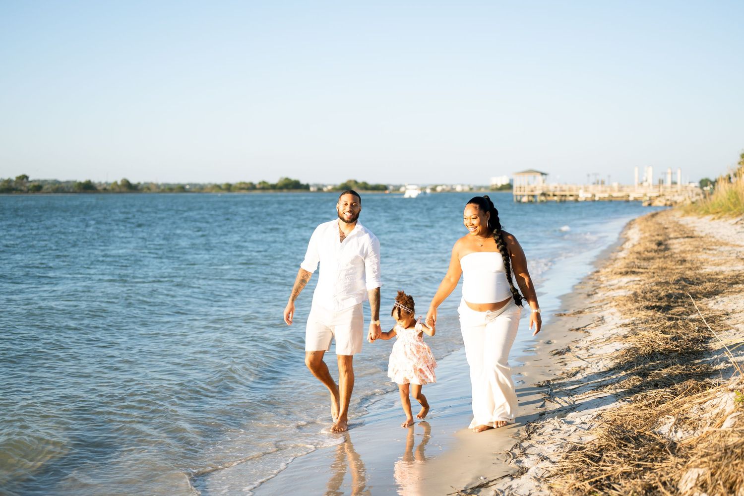 A family of four poses together on a beach with a pier in the background.