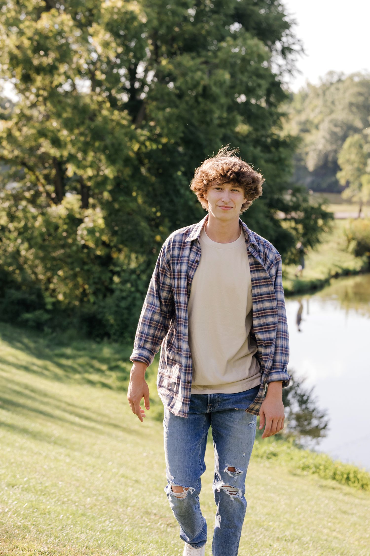 Casual summer style with plaid shirt and ripped jeans by a peaceful lake.