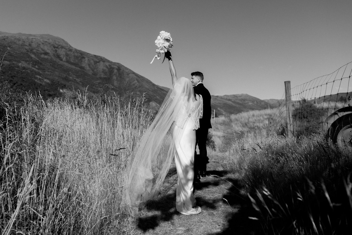 A black and white artistic wedding photograph showing a flowing dress blowing in the wind along a mountainside trail.
